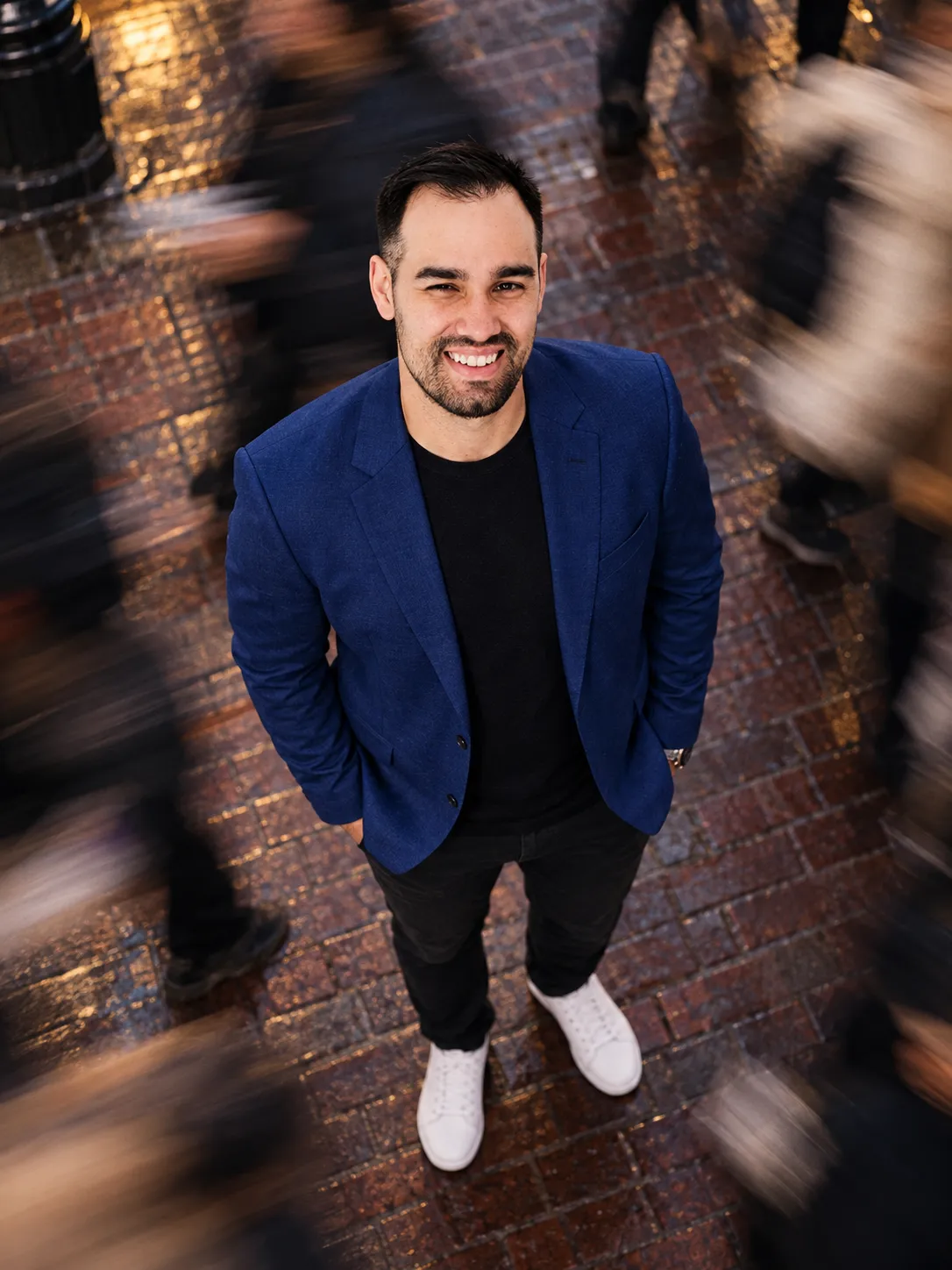 The same man in a royal blue blazer on a city sidewalk with a motion-blurred crowd