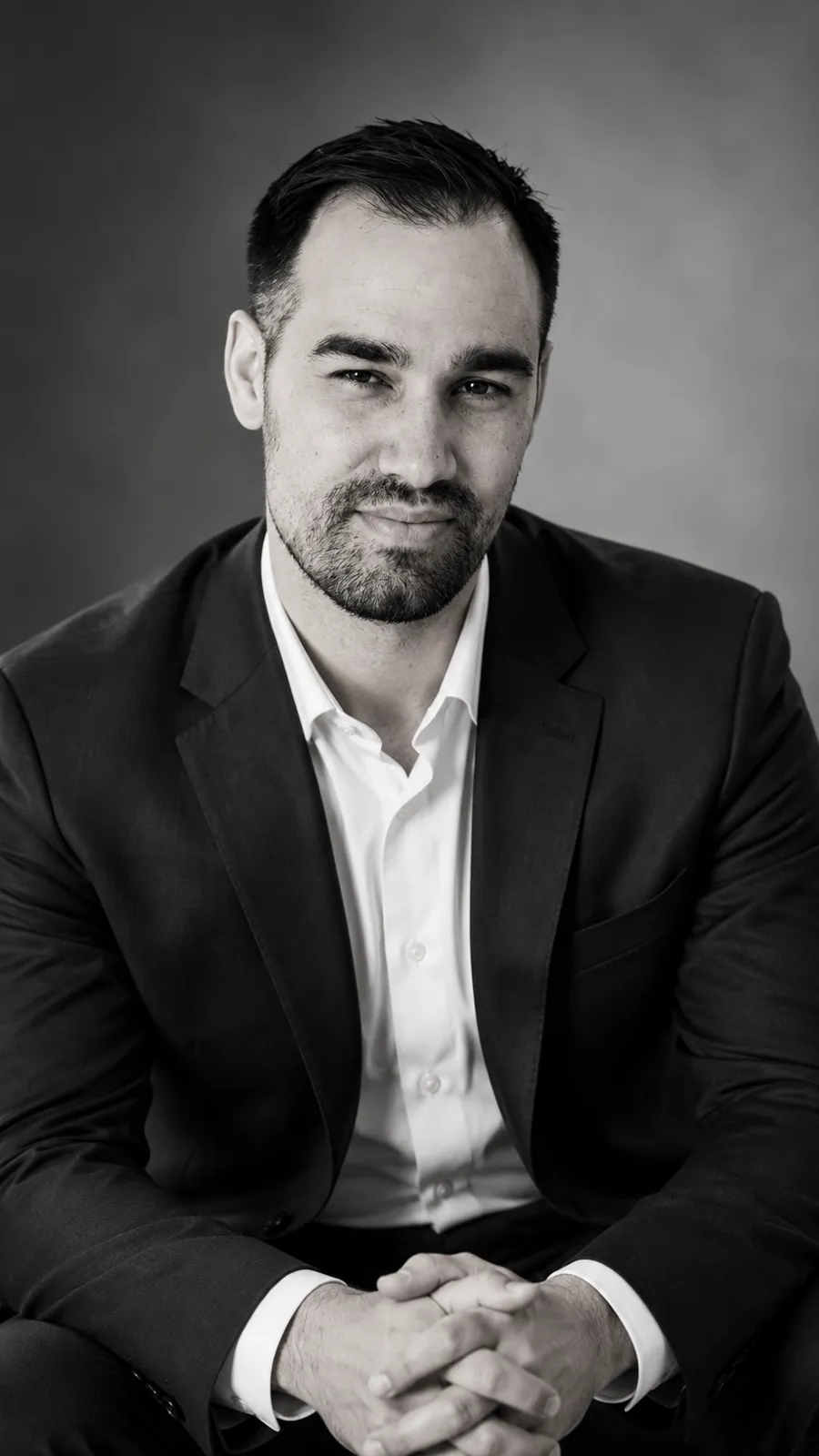 A dramatic black and white studio portrait in a dark suit
