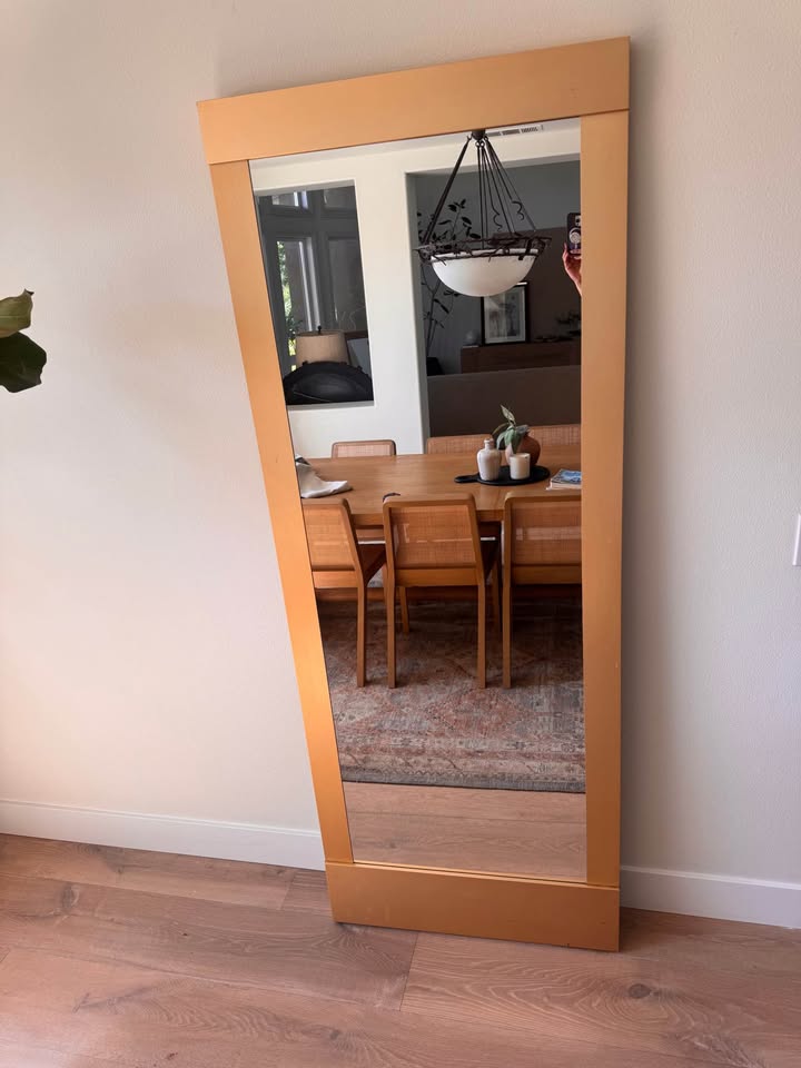 A wooden leaning mirror against a wall